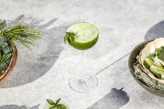 A bright green matcha ginger beer with basil in a tall cocktail glass.