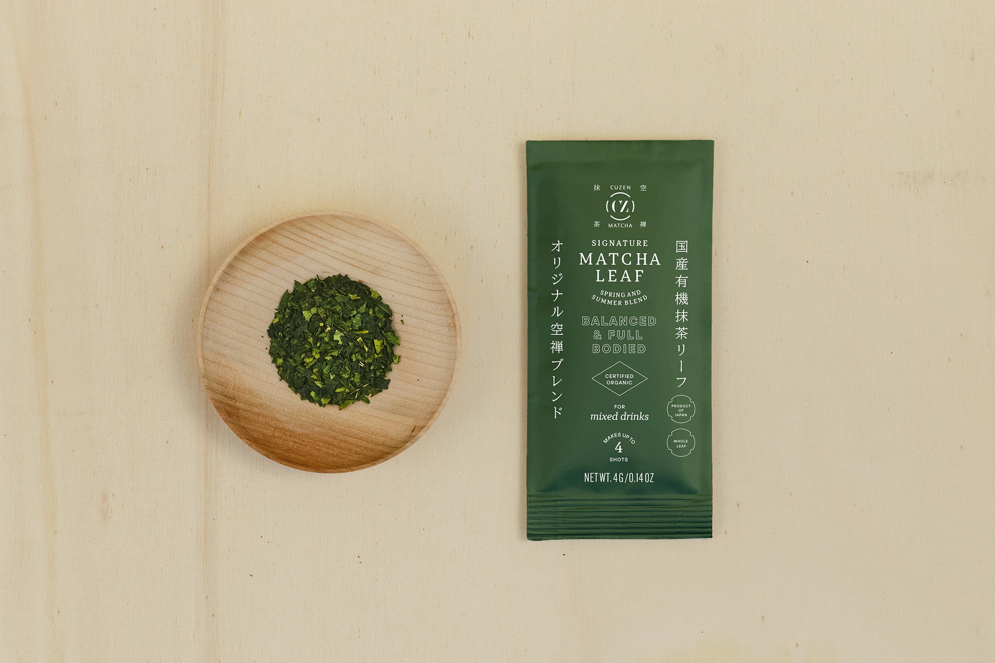 A 4-gram sample packet of Signature Blend Matcha next to a saucerful of deep green matcha leaves.