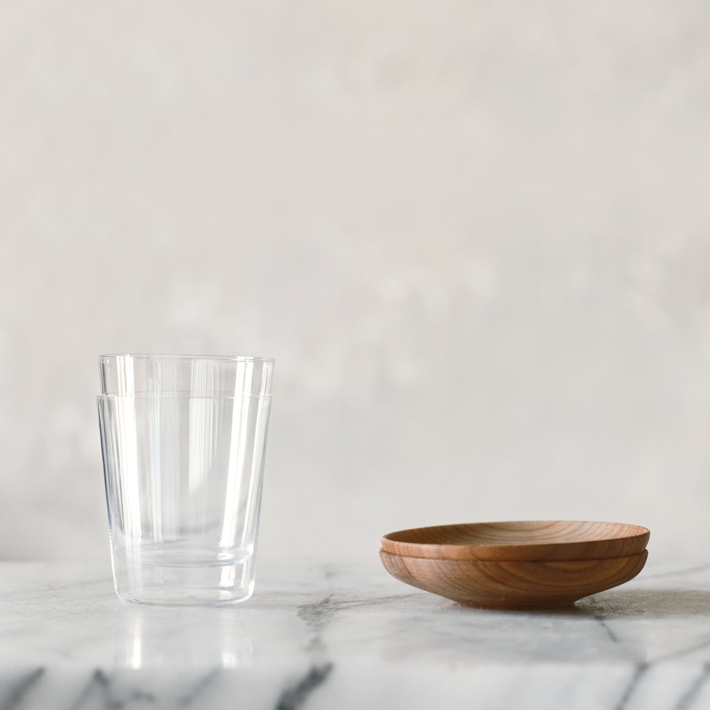 2 stacked Matcha Shot Glass next to 2 stacked Wooden Saucers on a marble countertop. 