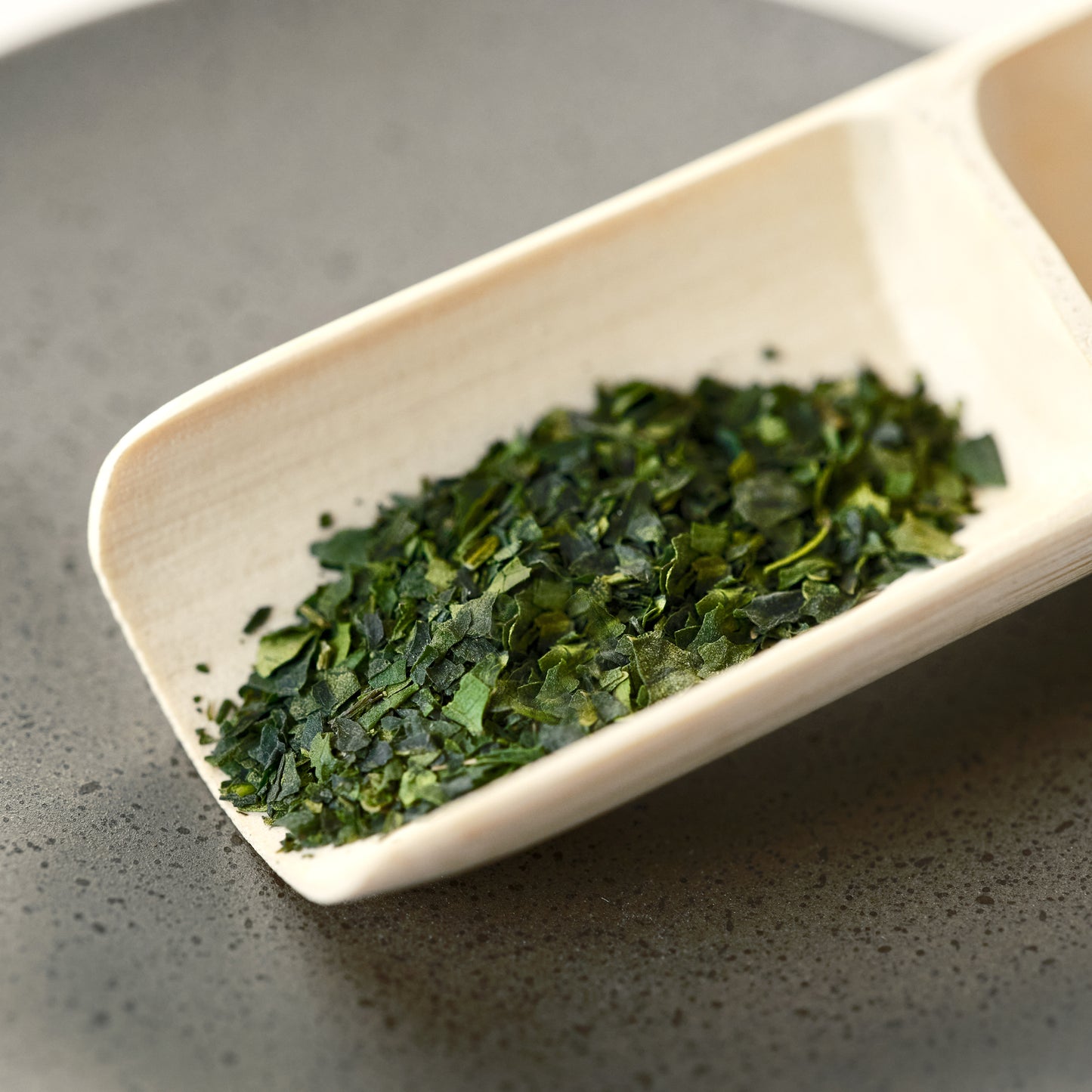 Dark green whole leaf matcha in a bamboo scoop.