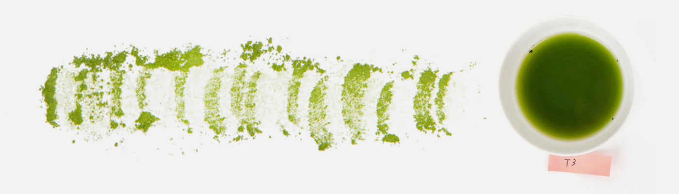 A line of bright green, freshly-ground matcha powder next to a bowl of deep green matcha. 