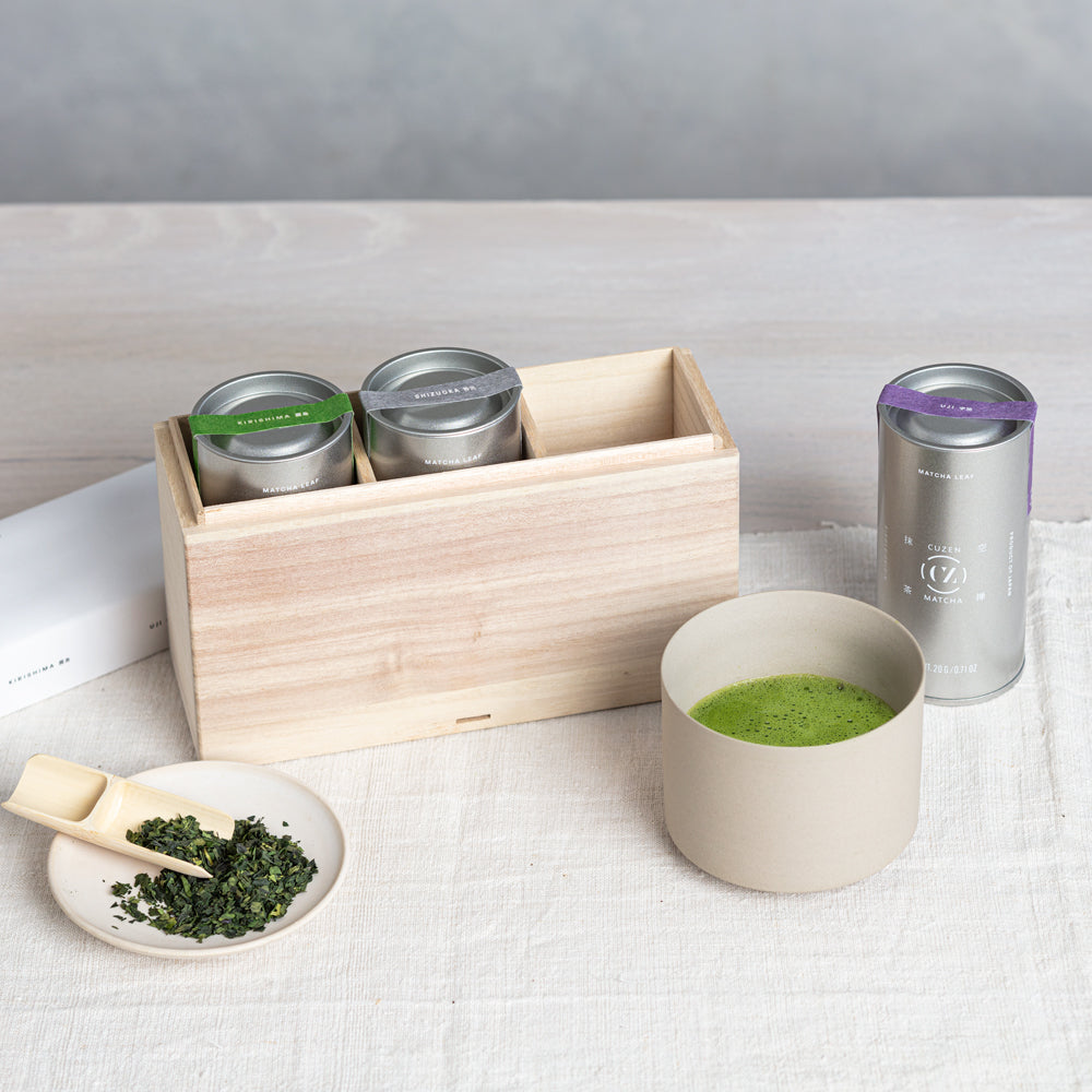 A Daily Matcha Bowl of frothy matcha, a kiri bako holding two Cuzen Single Origin whole leaf tea canisters, a third canister sitting nearby.