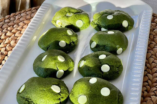 Eight vibrant green brown butter matcha cookies with starkly contrasted white chocolate chips, displayed on a white platter.