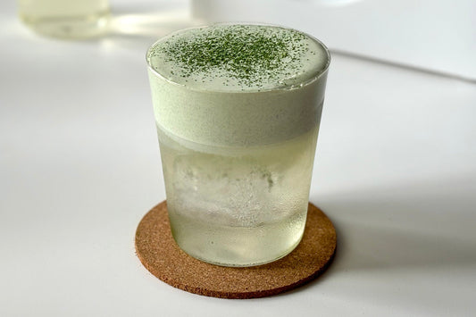 A glass of coconut water topped with a foamy matcha cream and dusted with matcha powder.