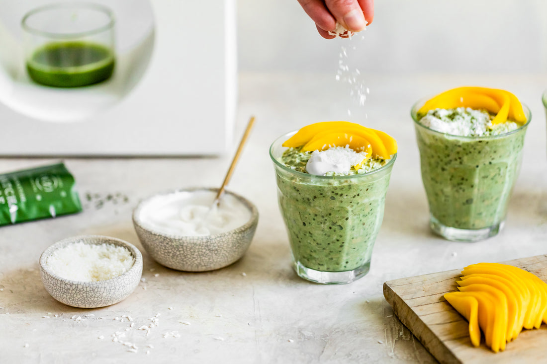 Two glasses of vivid green coconut matcha latte overnight oats, garnished with yogurt and mango slices.