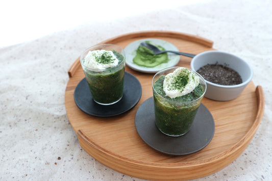 Two glass cups full of creamy matcha chia pudding, topped with whipped cream and sprinkled with matcha powder.