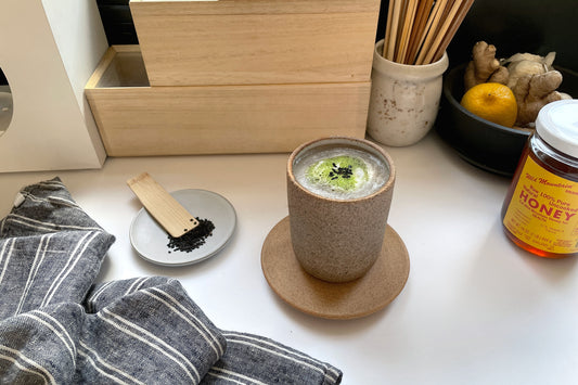 A mug of hot, foamy-black sesame matcha latte, sprinkled with black sesame seed.