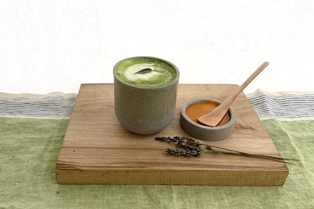 A warm cup of frothy garden matcha latte in a stone-colored cup, next to a sprig of fresh lavender.