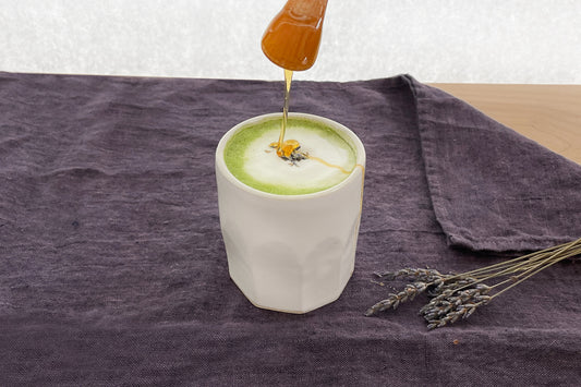 A cup of warm honey lavender matcha latte with a decorative sprinkle of lavender and a drizzle of honey.