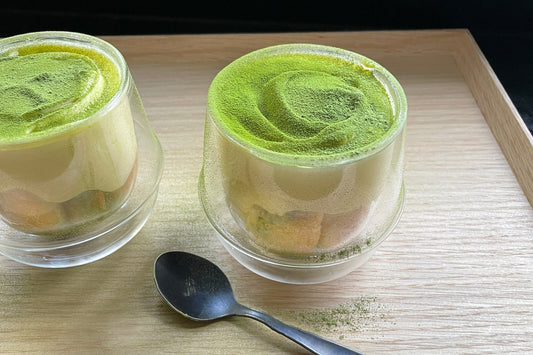 Two glass cups of matcha tiramisu, dusted with bright green freshly-ground matcha powder.