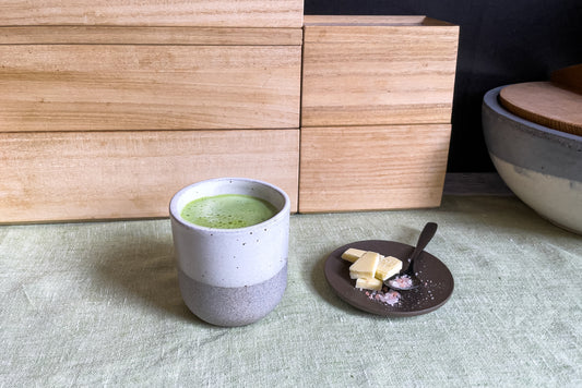 A frothy white chocolate matcha in a Perfect Matcha Latte Cup, next to a plate of hard cheese and sea salt.