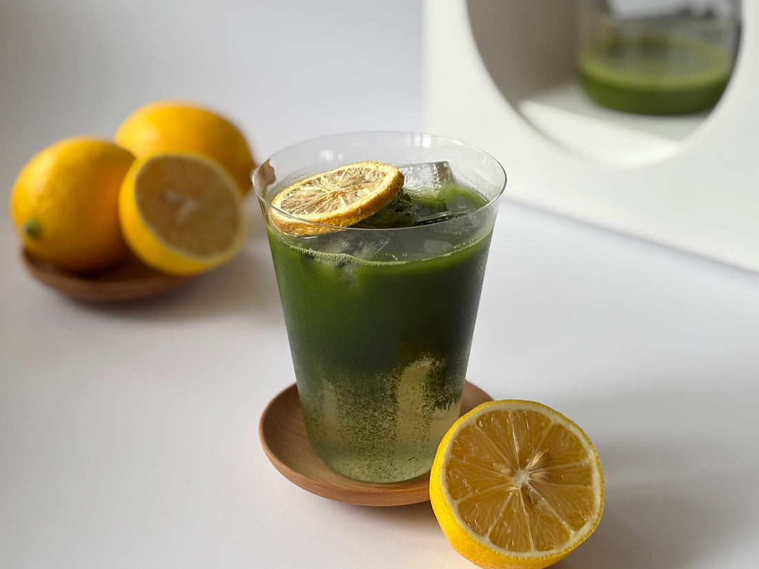 A bright greet and yellow matcha lemonade, flanked by fresh lemon halves and a Matcha Maker.