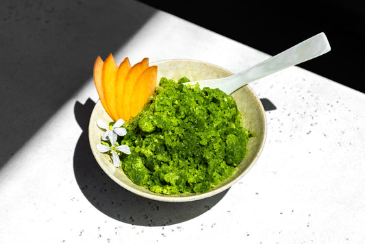 A bowl of bright green shaved ice, garnished with edible flowers and fruit.