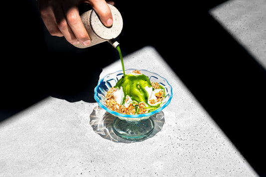 A bright green shot of matcha is drizzled over a scoop of vanilla ice cream with almond praline crumbled over the top.