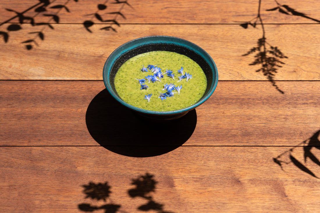 A bowl of jade-colored matcha tapioca, garnished with purple flowers.