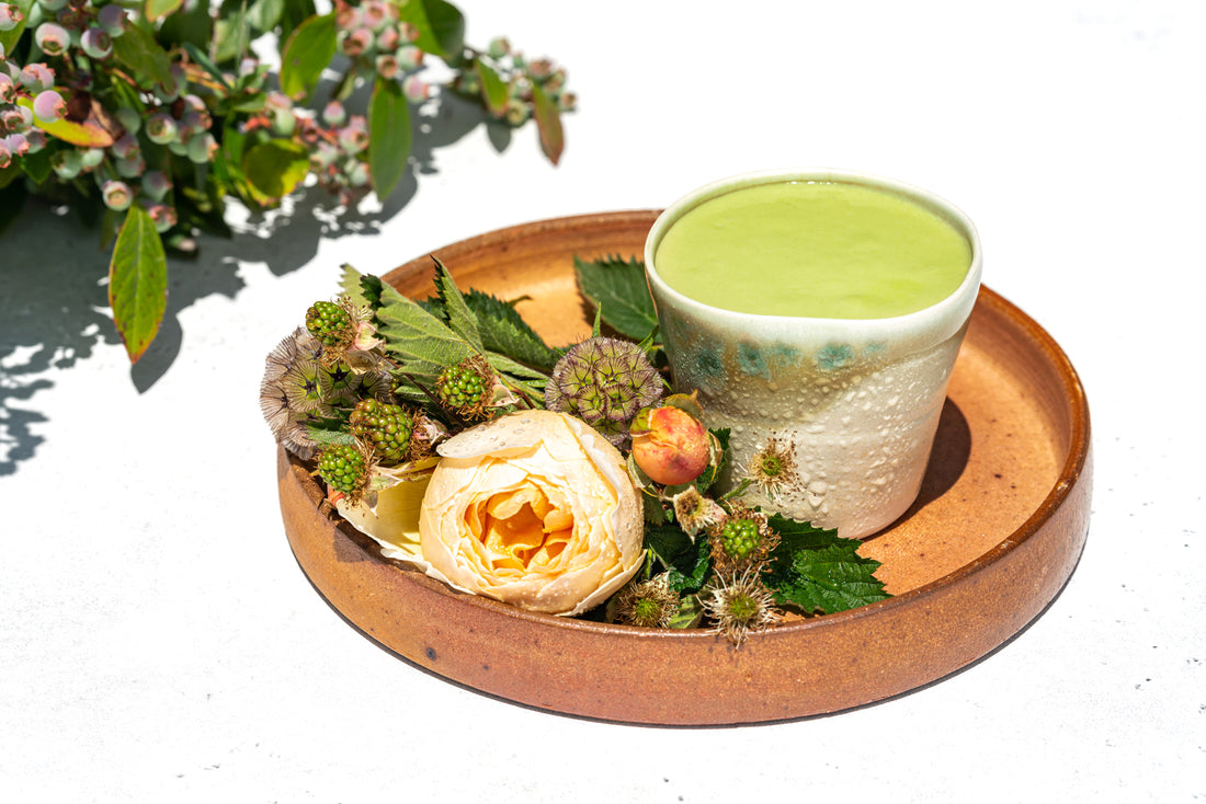 A smooth matcha mango lassi, cool with condensation on the outside of the ceramic cup, surrounded by a summer bouquet.