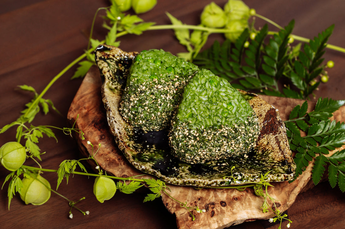 Two triangle onigiri made with matcha, peas, and tencha goma shio, nestled on a wooden plate.