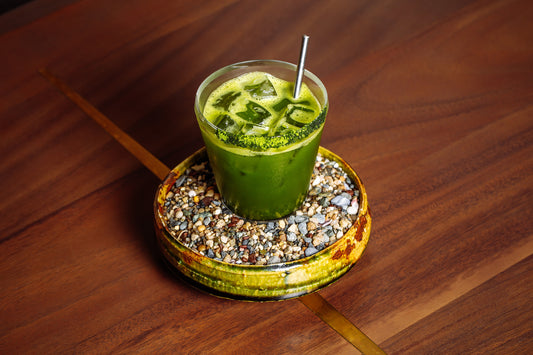 A festive bright jade-colored mocktail in a small glass sitting in a saucer full of colorful stones.