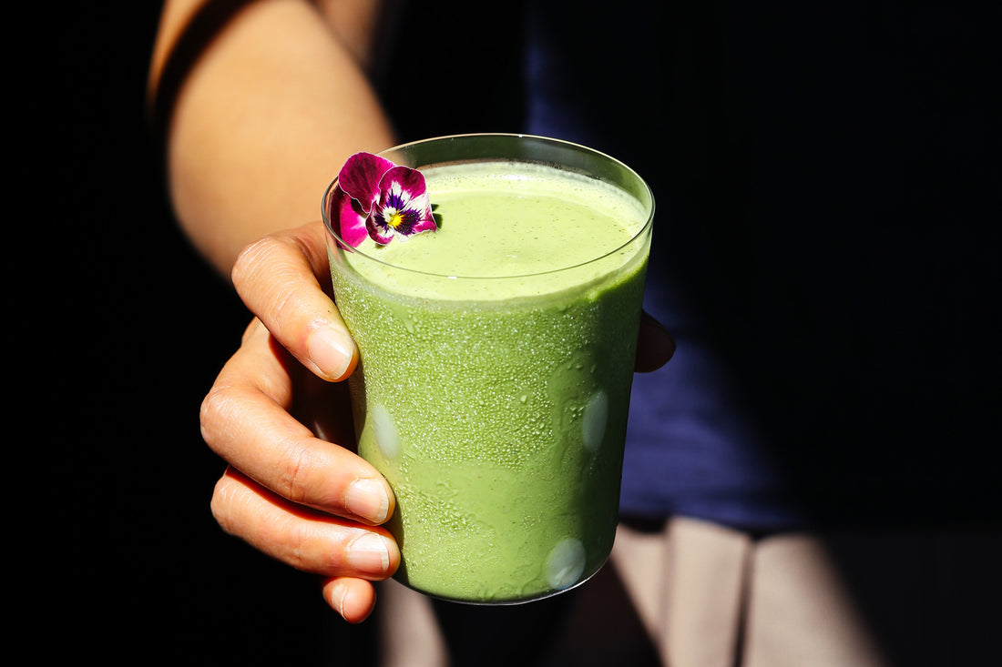 A matcha-bright, frothy smoothie, garnished with a pretty red flower.