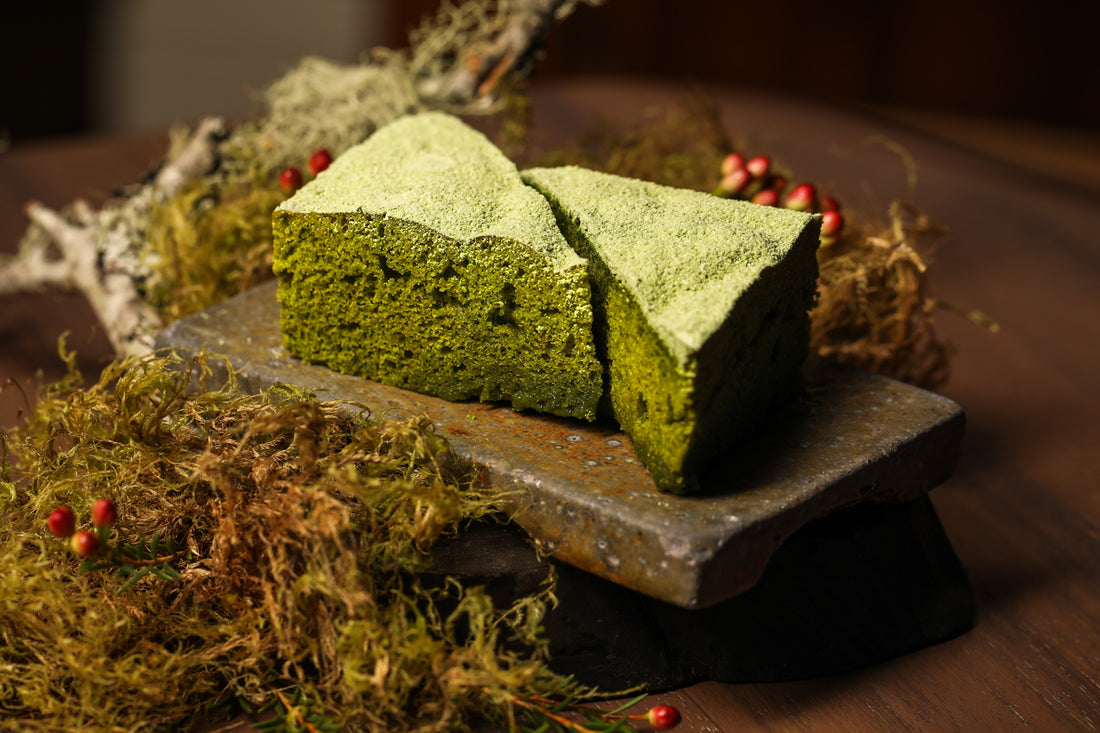 Two triangular, spongy green matcha steam cakes, facing each other on a wooden board.