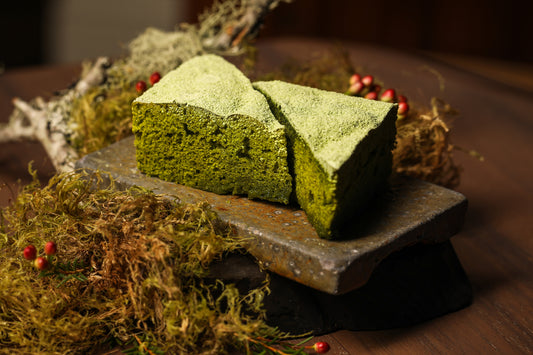 Two triangular, spongy green matcha steam cakes, facing each other on a wooden board.