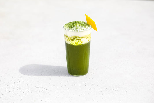 A glass of bright green, sparkling yuzu matcha topped with cream and sprinkled with matcha powder.