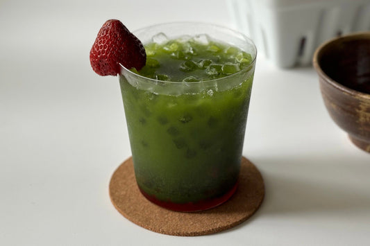 An iced strawberry matcha drink, garnished with a fresh strawberry.