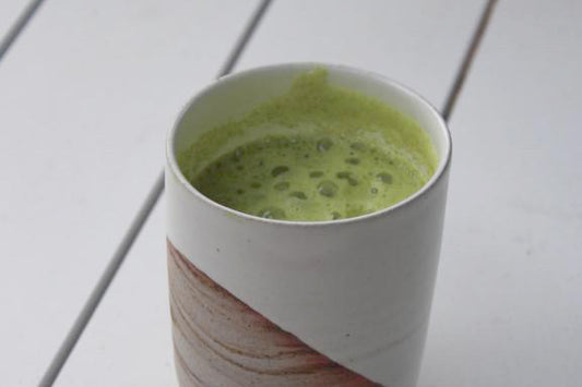 A frothy green turmeric matcha latte in a partially glazed ceramic mug.