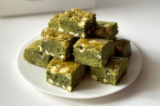 A stack of green-tinted, dense matcha brownies with white chocolate chips.