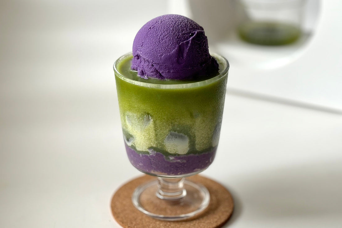 A stemmed dessert cup layered with bright green and purple layers of ube jam, matcha latte and ube ice cream.