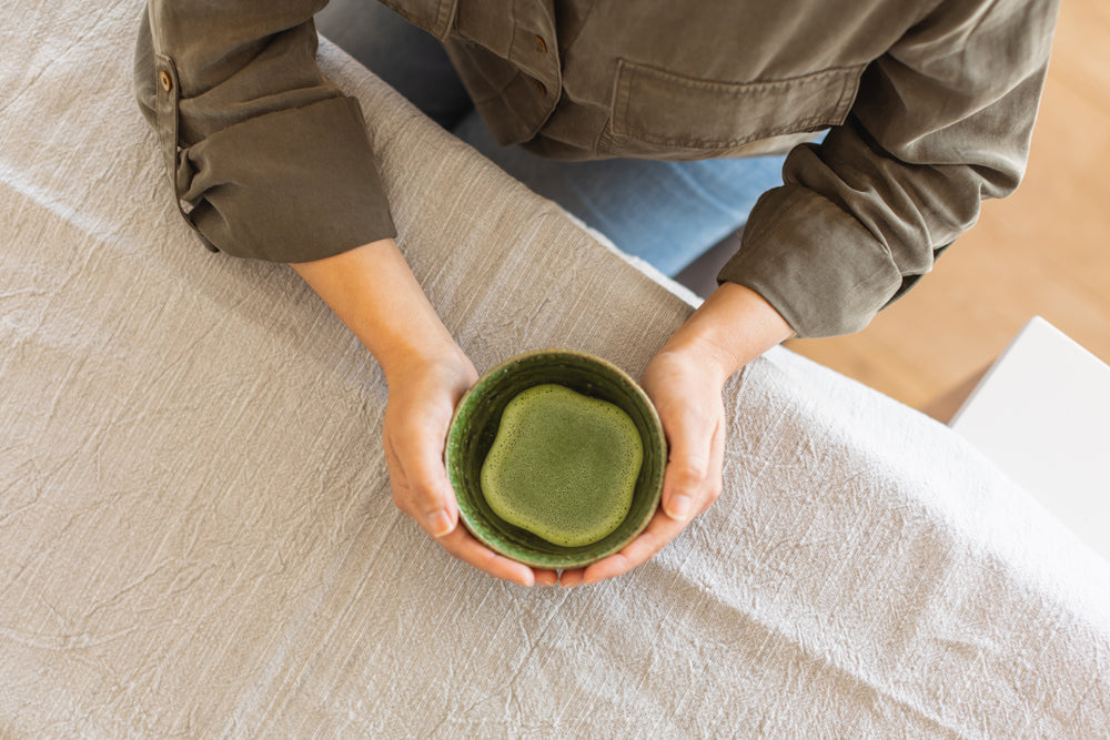 Bird’s eye view of a person’s arms, both hands resting comfortably around the cup of matcha.