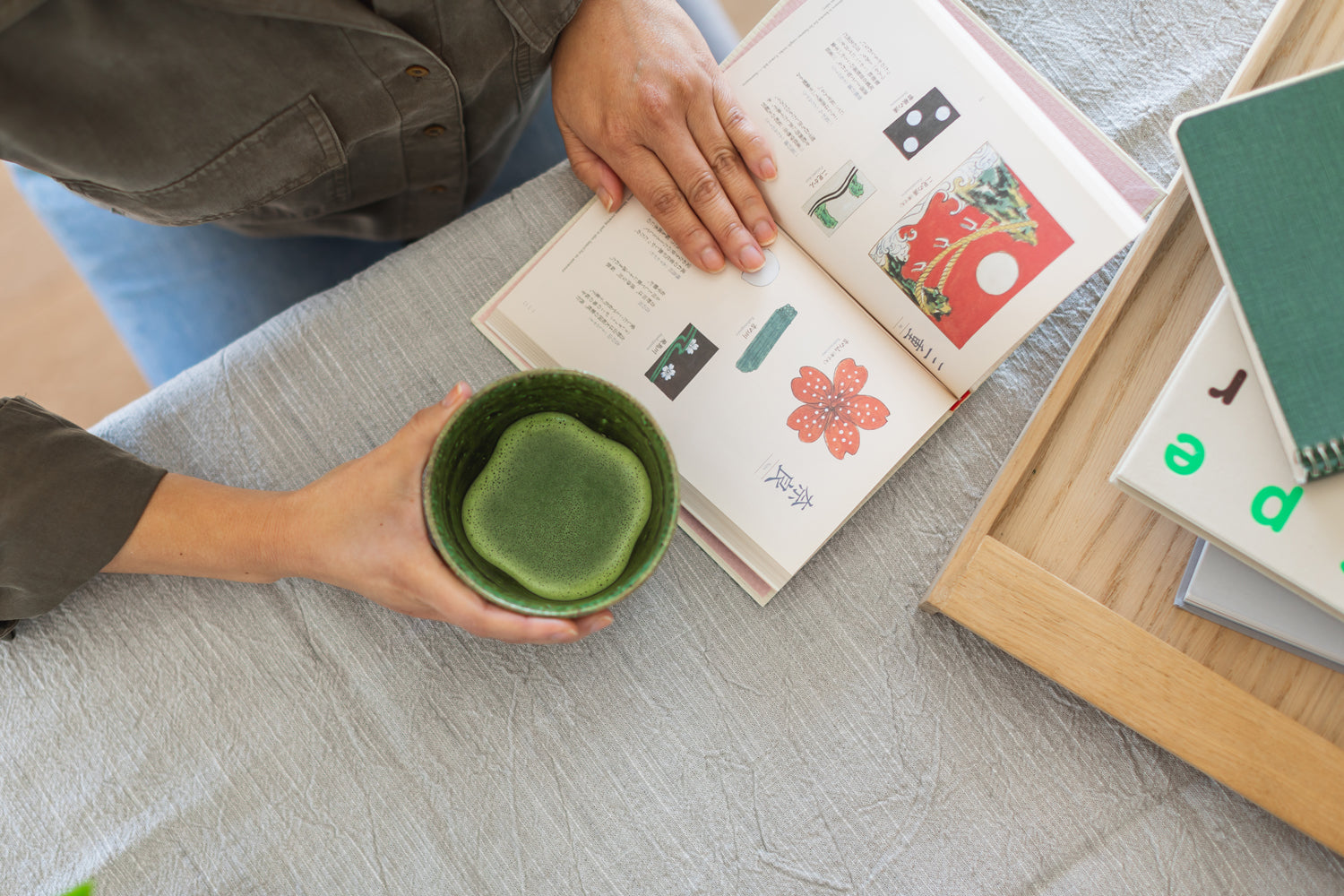Bird’s eye view of a person enjoying a bright green cup of matcha and a colorful book.