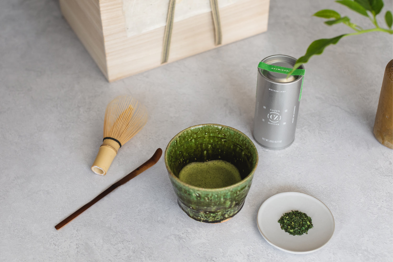 The Cuzen Ceremonial Set displayed on a table: Single Origin tea, a green matcha bowl, a bamboo whisk and a bamboo scoop.