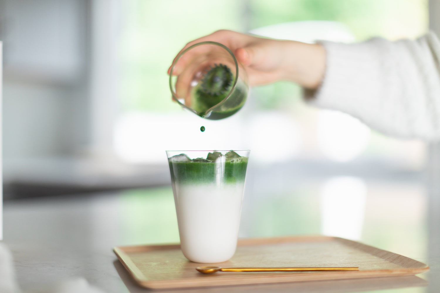 A freshly-ground matcha shot being poured into a glass of milk in our Cuzen Perfect Matcha Latte Glass.