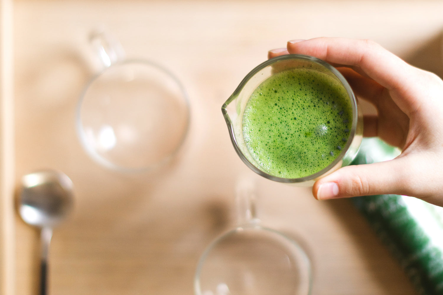 A hand holds a whisking cup full of a frothy, bright green matcha shot.