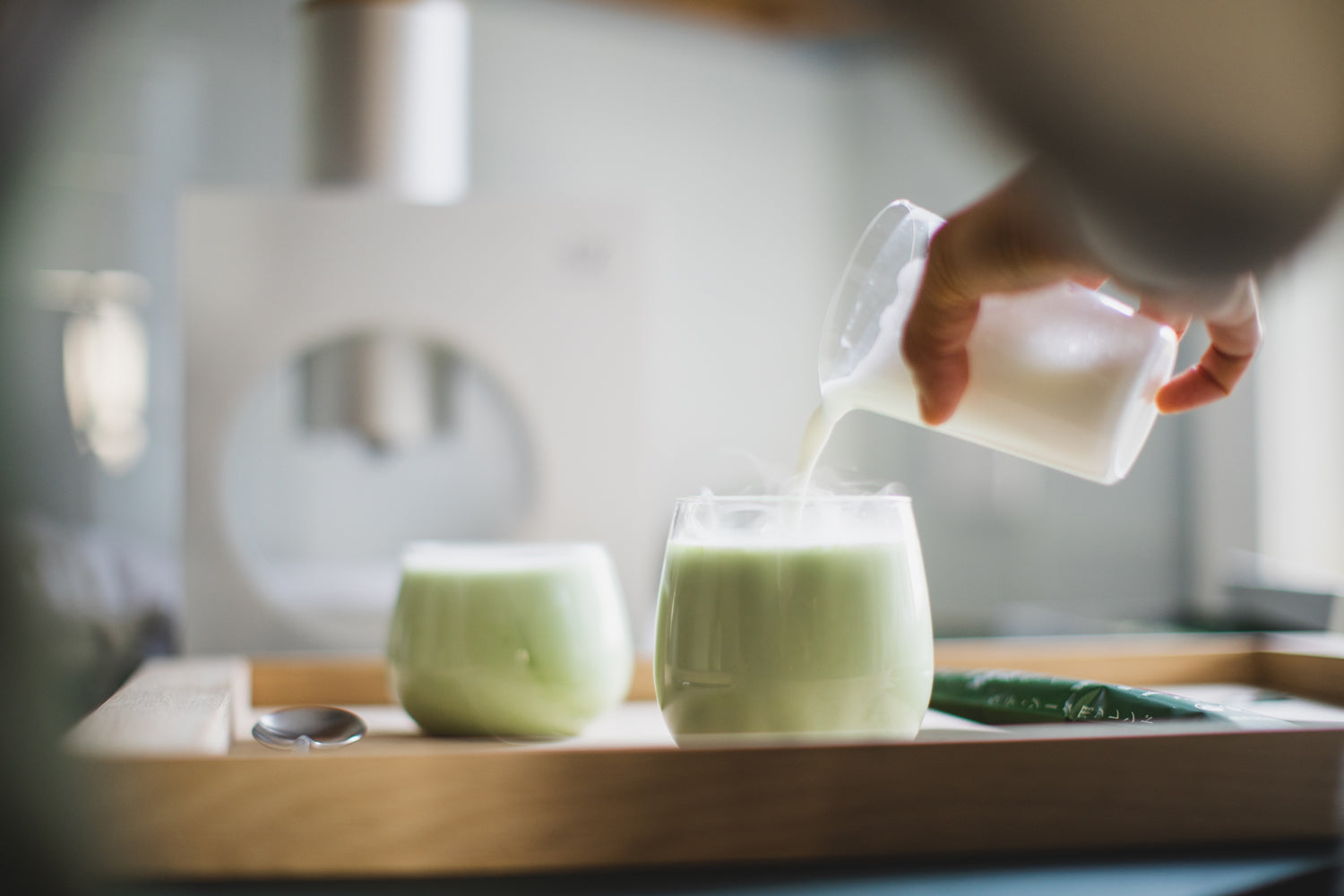A person pours milk into a glass cup, making a perfect cup of matcha latte.