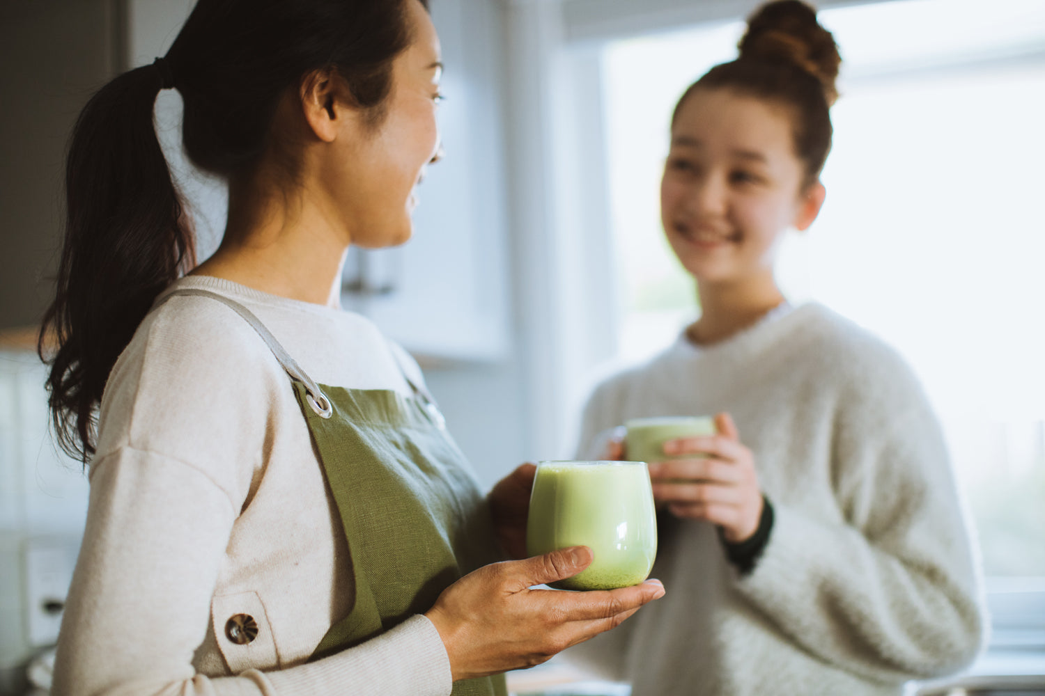 Two women smile and chat, sipping matcha lattes made with freshly-ground matcha.
