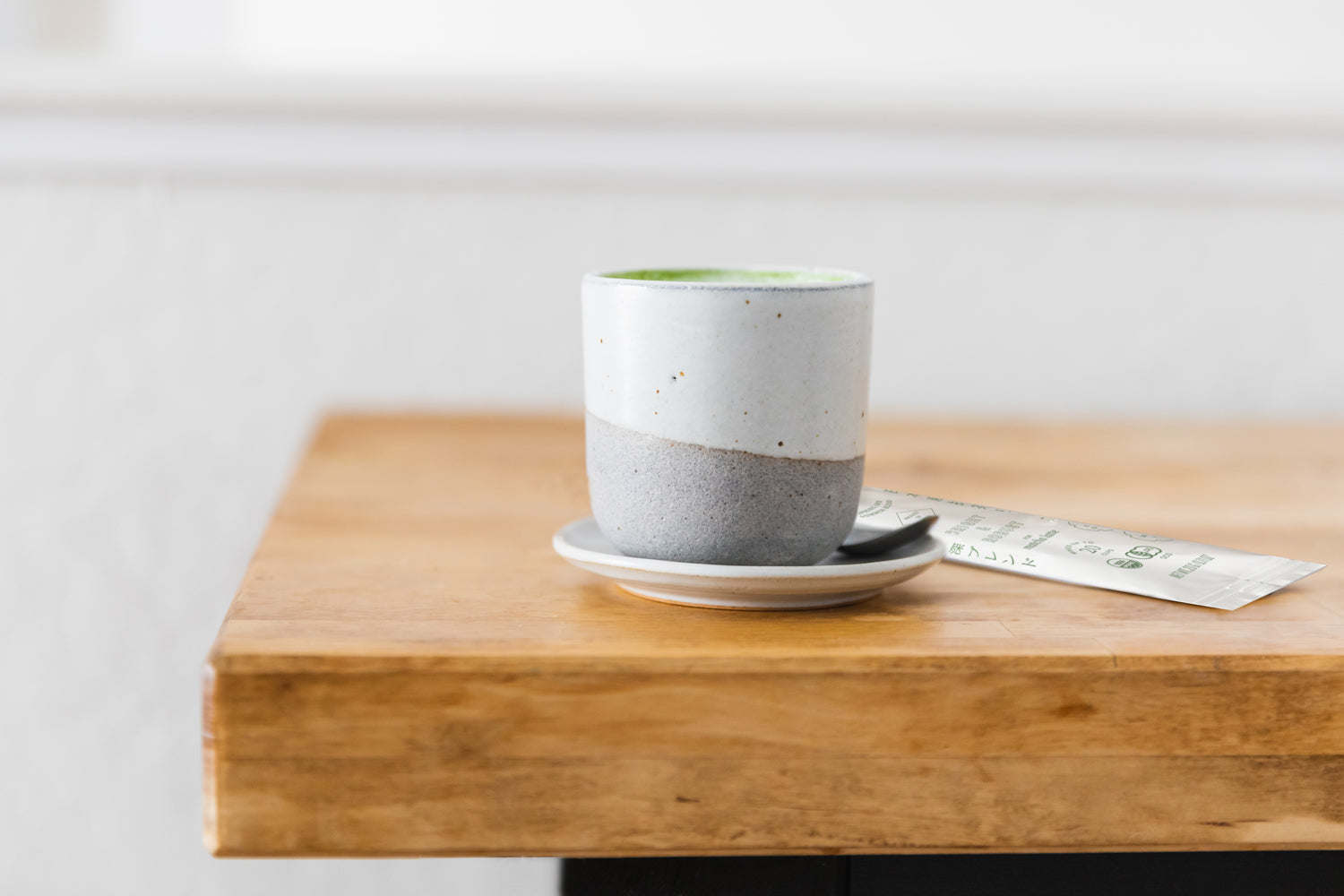 Cuzen’s Perfect Matcha Latte Cup full of a warm matcha latte, next to a packet of whole Latte Blend Matcha Leaf.