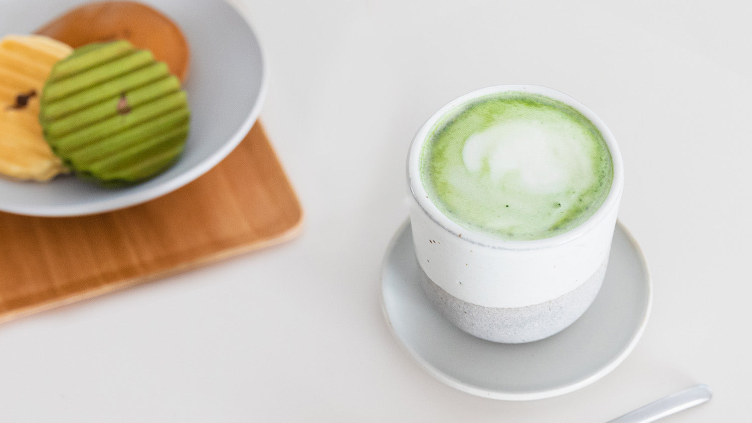 A frothy cup of matcha latte in our Perfect Matcha Latte Cup, next to a plate of cookies.