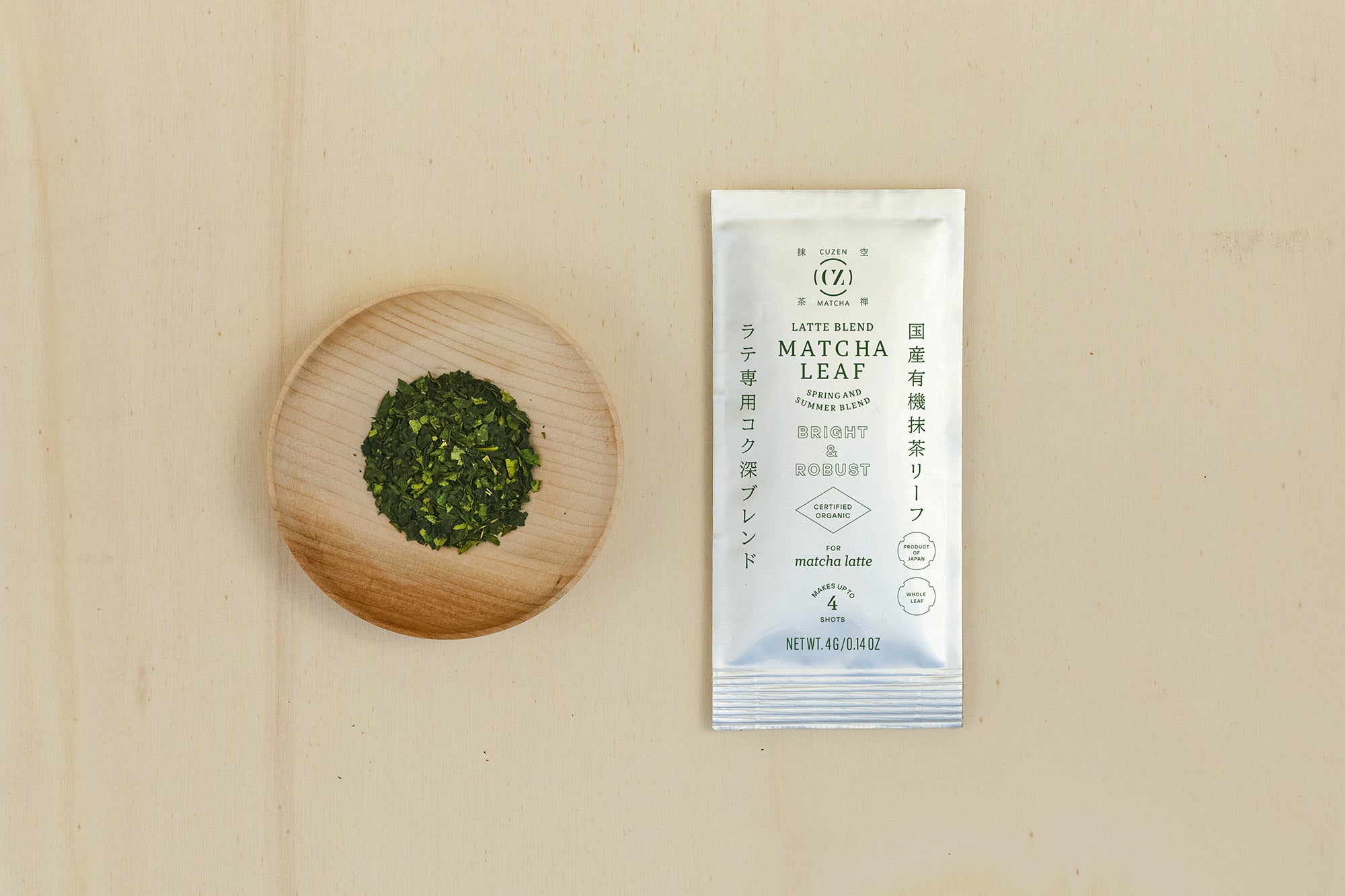 A 4-gram sample packet of Latte Blend Matcha next to a saucerful of deep green matcha leaves.