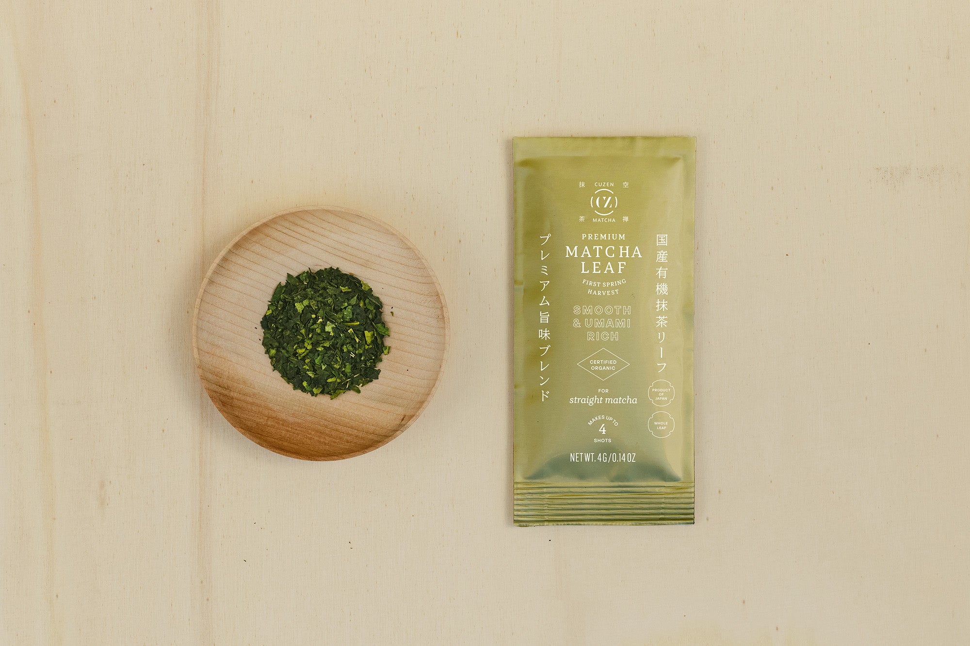 A 4-gram sample packet of Premium Blend Matcha next to a saucerful of deep green matcha leaves.