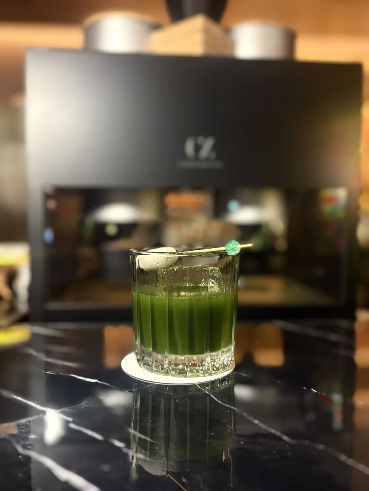 A matcha cocktail, set on a surface at Toshiro's Bar. The Cuzen Matcha Maker Pro is in the background.