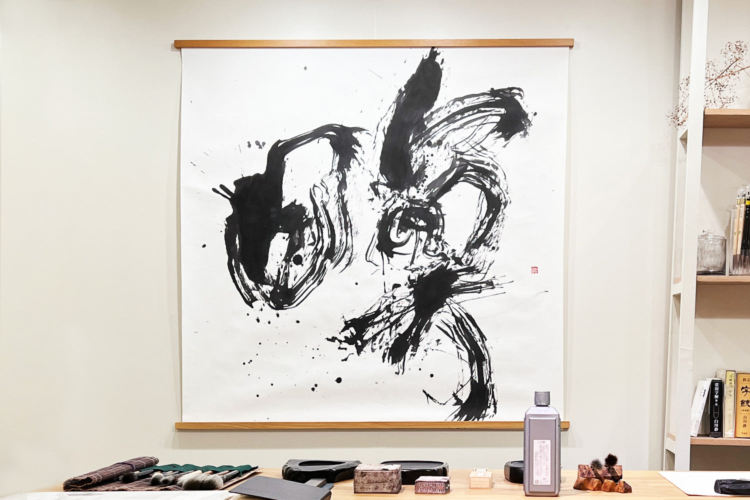 A calligraphy piece by Aoi Yamaguchi, entitled “Meditate” hangs on the wall behind a table display of brushes, ink and other equipment in her studio.