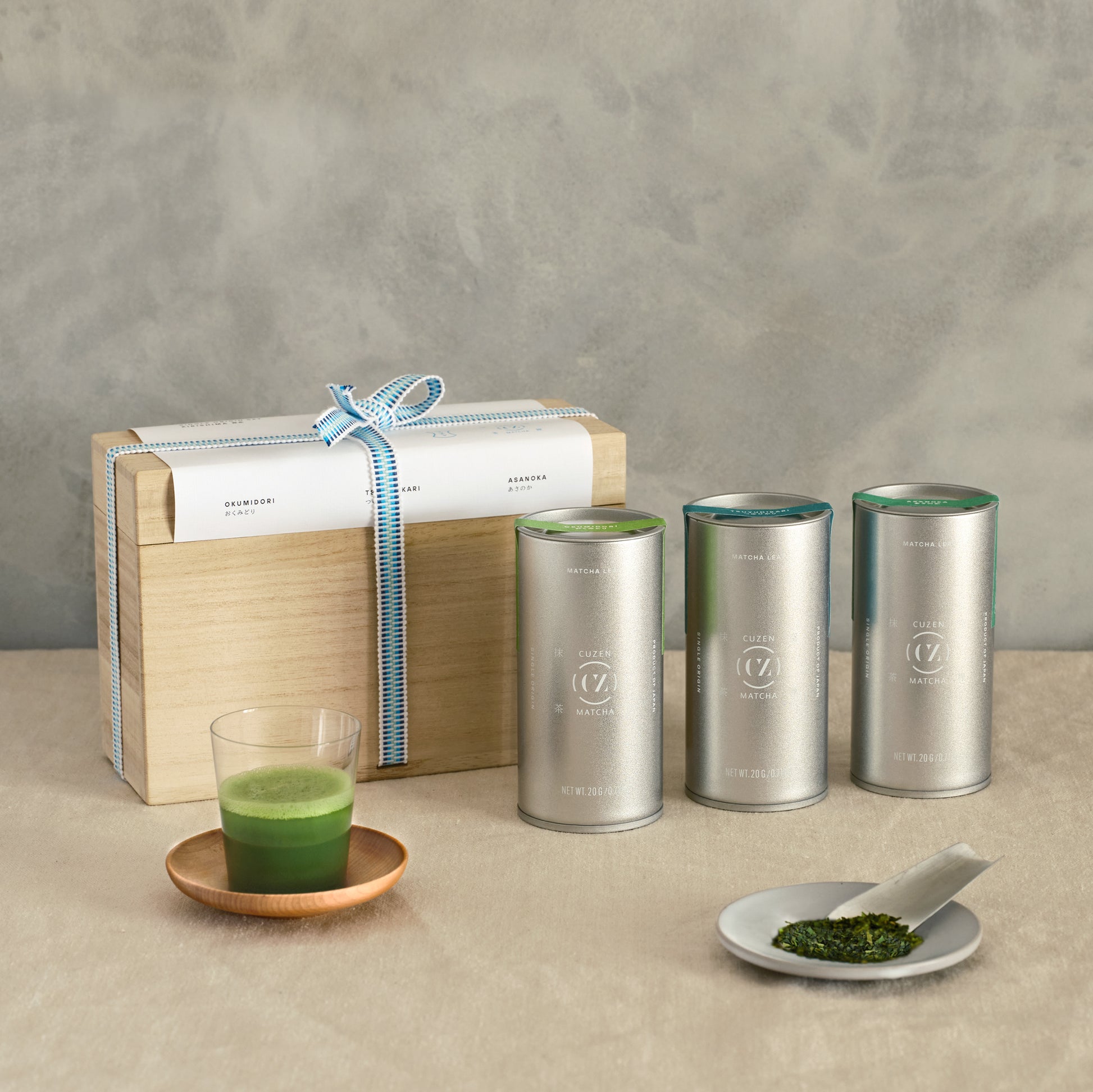 Three canisters of Single Origin Matcha in front of the kiri bako and a saucer of deep green whole leaf matcha.
