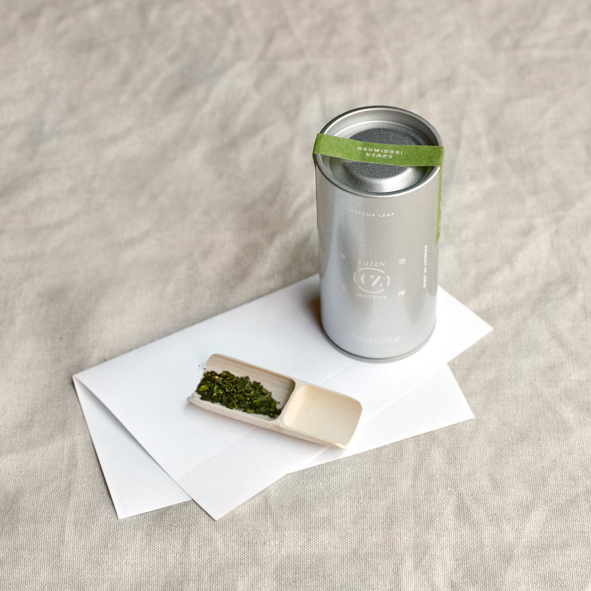 A canister of Okumidori Single Origin Matcha Leaf from Kirishima, next to a bamboo scoop of Matcha Leaf. 