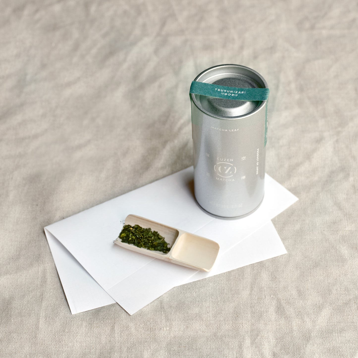 A canister of Tsuyuhikari Single Origin Matcha Leaf from Kirishima, next to a bamboo scoop of Matcha Leaf. 