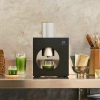 Matcha Maker Sumi Black, flanked by bright green iced matcha drinks and packets of whole leaf matcha.