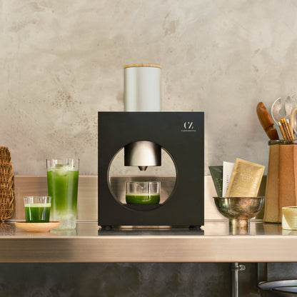 Matcha Maker Sumi Black, flanked by bright green iced matcha drinks and packets of whole leaf matcha.