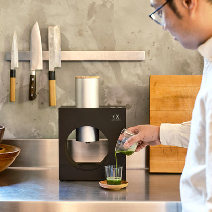 A person pours a matcha shot from the whisking cup into a glass that is set in front of the Sumi Black.