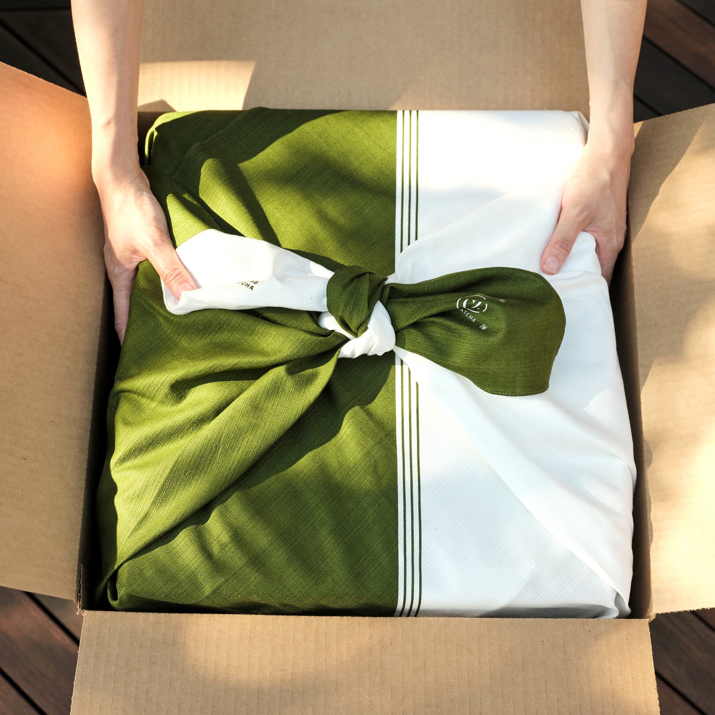 Two hands pull the Matcha Maker Gift Starter Kit, wrapped in the traditional style with a furoshiki wrap, out of a box.